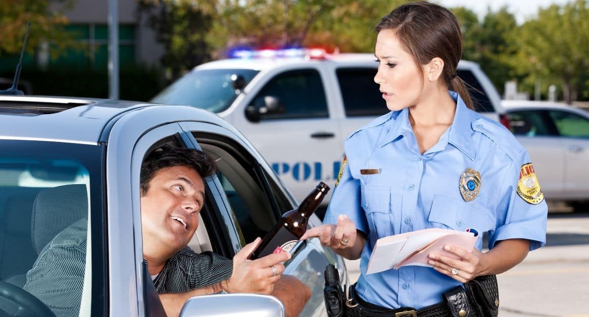 Police officer conducting a DUI traffic stop in Georgia, speaking with a driver holding a bottle beside a patrol SUV